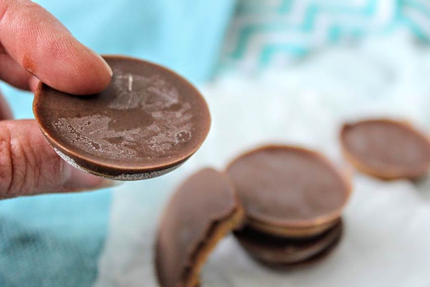 Hand holding keto peanut butter cup between finger and thumb with a stack of peanut butter cups in the background