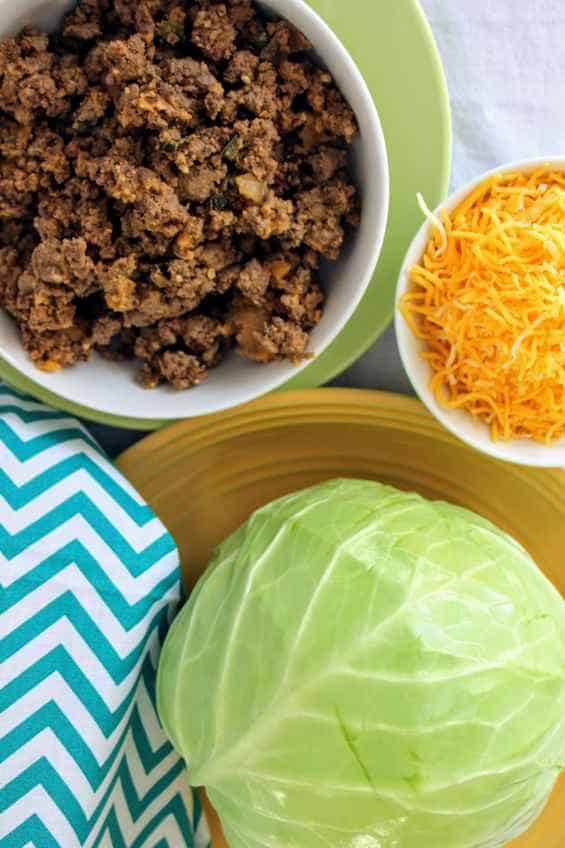 Whole head of cabbage with bowl of taco meat and bowl of shredded cheese, with a napkin next to it.