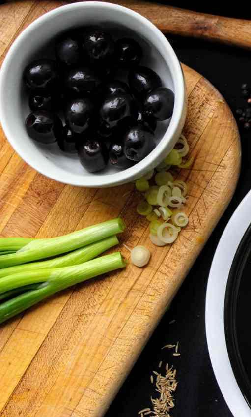 Overhead shot of bowl of black olives on cutting board with green onions