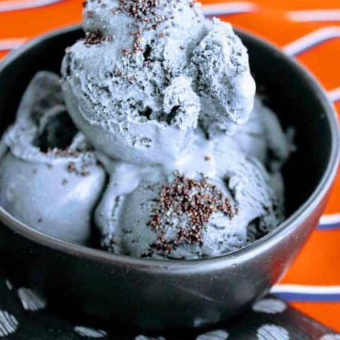 Creamy black ice cream sprinkled with black poppy seeds in a decorative black bowl on colorful napkins