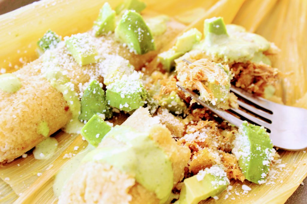 Closeup of keto low carb almond flour tamales on corn husk with tomatillo dressing and avocados